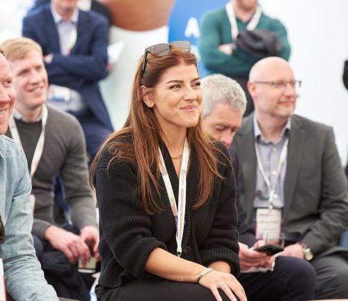 A group of people sat in the audience smiling towards the stage (off frame) at a conference