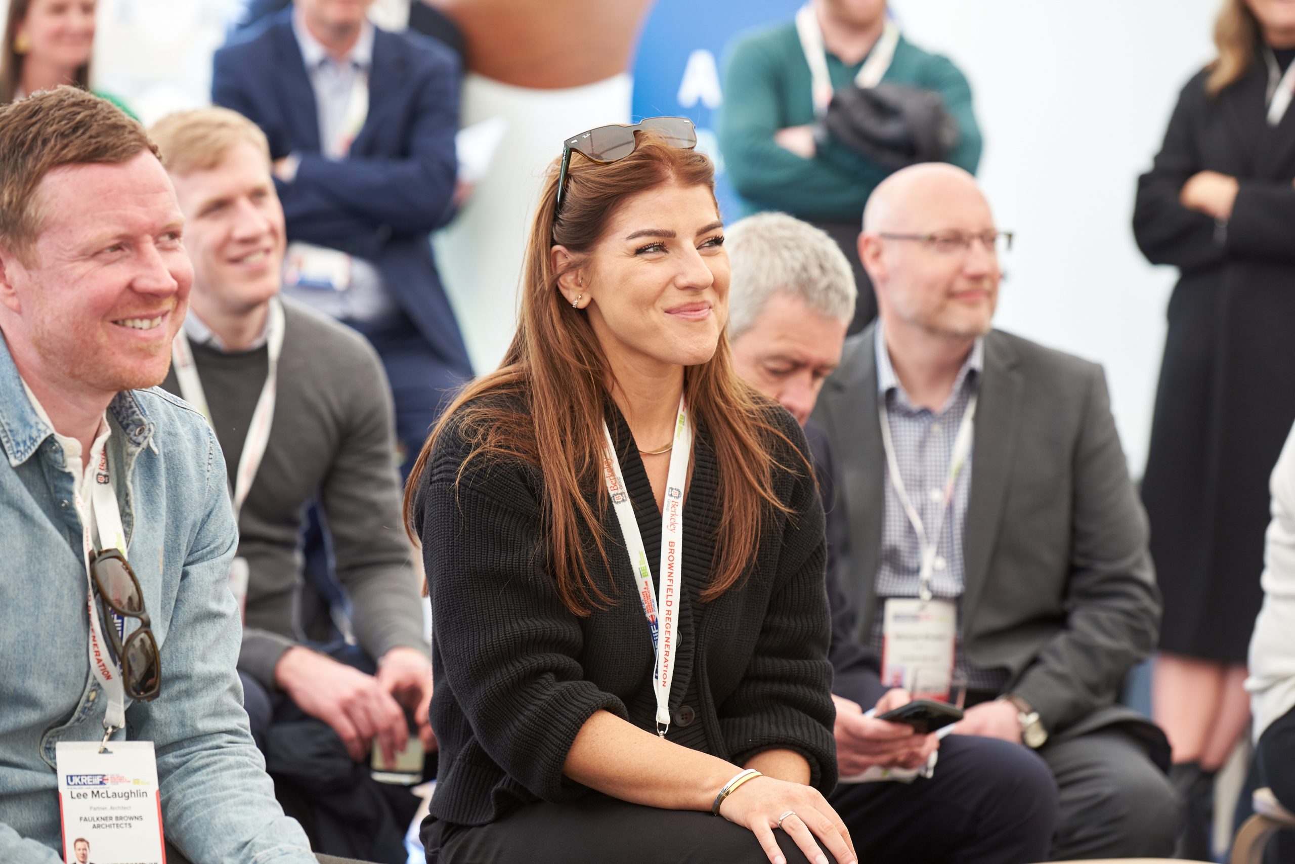 A group of people sat in the audience smiling towards the stage (off frame) at a conference