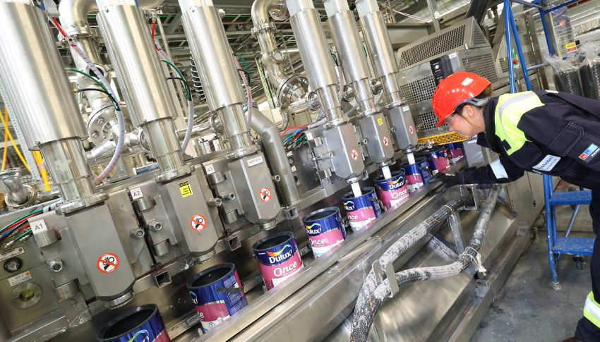 Person in a paint factory wearing a hard hat and protective clothing monitoring the machine.