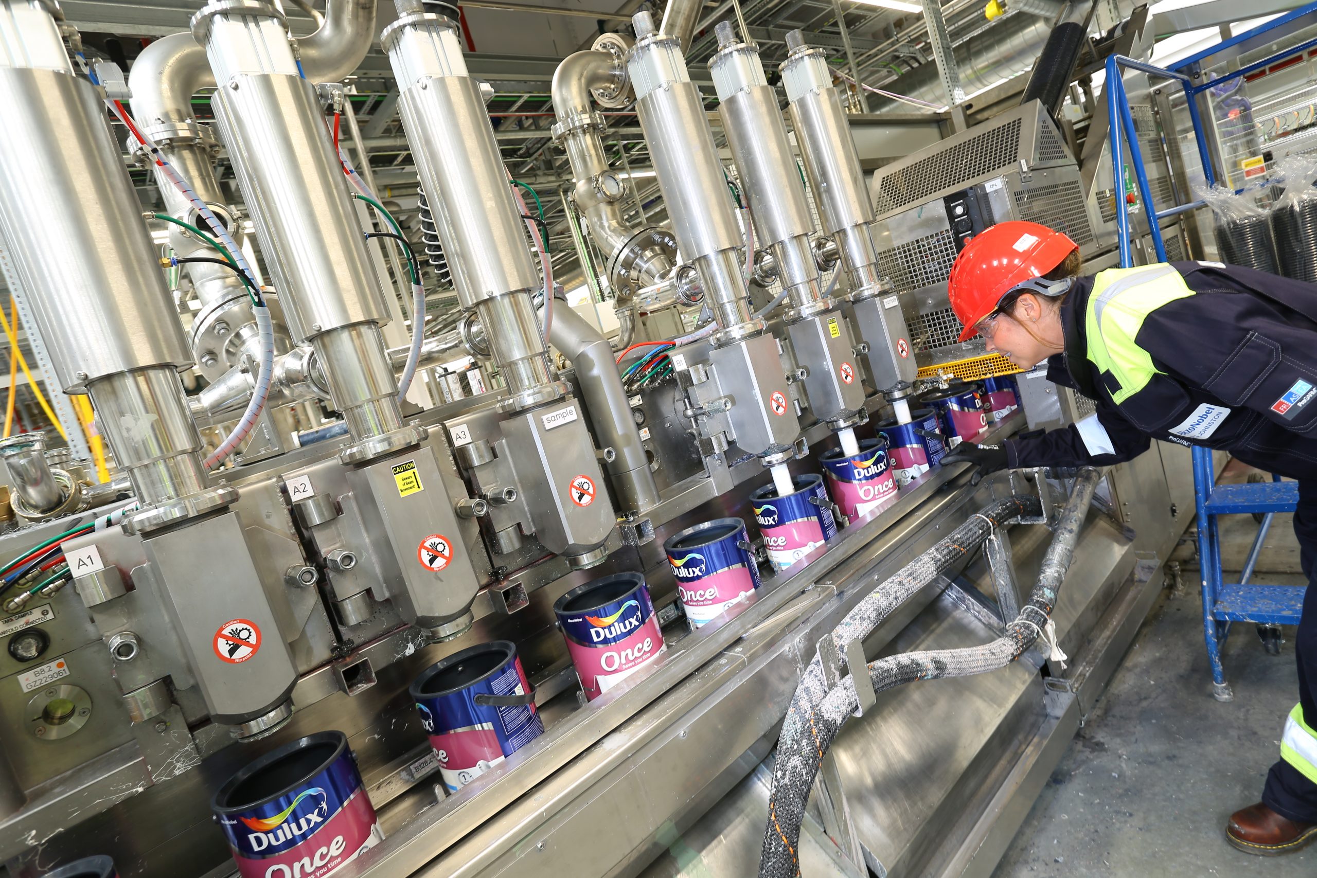 Person in a paint factory wearing a hard hat and protective clothing monitoring the machine.